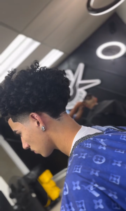 Client with tight curls and a clean burst taper behind the ear