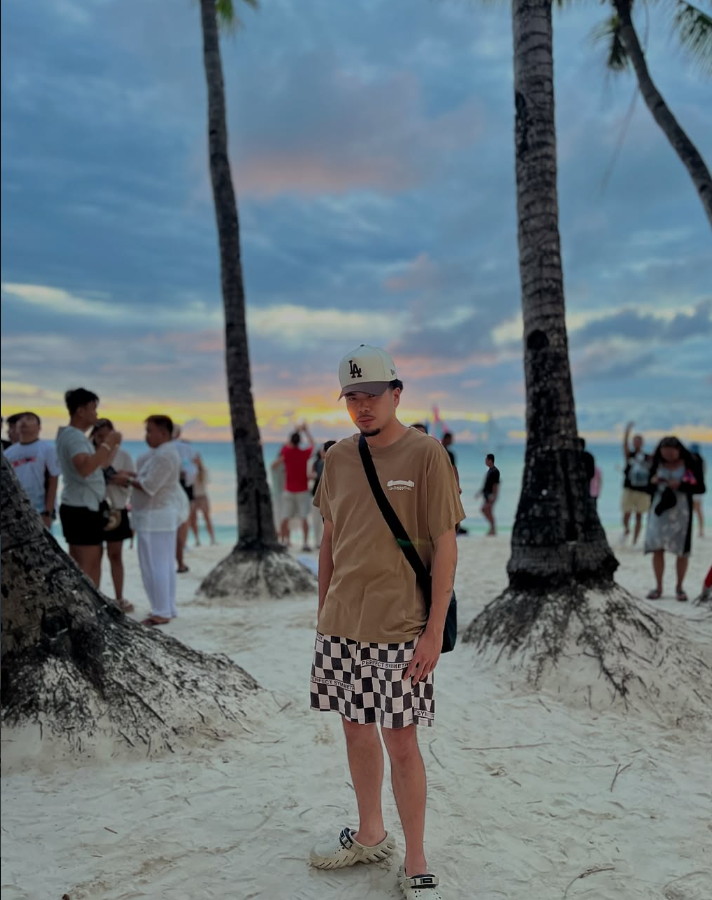 Jordan Cruz standing on a beach at sunset in a tan tee and checkered shorts